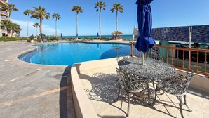 A swimming pool with lounge chairs and umbrellas, surrounded by palm trees and a view of the ocean. - Wake Up to the Sea Oceanfront Retreat W207 (Puerto Peñasco)