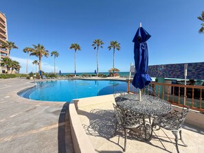 A swimming pool with lounge chairs and umbrellas, surrounded by palm trees and a view of the ocean. - Wake Up to the Sea Oceanfront Retreat W207 (Puerto Peñasco)
