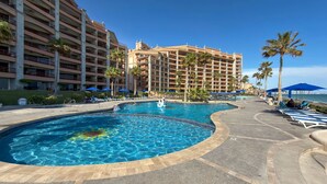 A hotel pool area with a large pool, lounge chairs, and palm trees. - Wake Up to the Sea Oceanfront Retreat W207 (Puerto Peñasco)