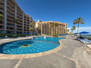 A hotel pool area with a large pool, lounge chairs, and palm trees. - Wake Up to the Sea Oceanfront Retreat W207 (Puerto Peñasco)