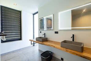 Ein modernes Badezimmer mit zwei Waschbecken, einem großen Spiegel und einem Fenster mit Jalousien.