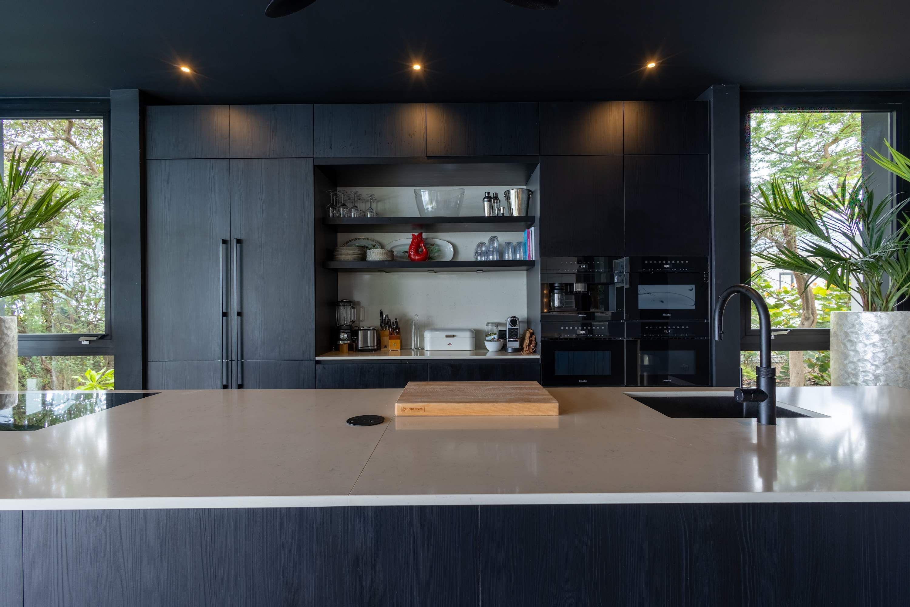 Una cocina moderna con una isla central, electrodomésticos integrados y vistas al exterior.