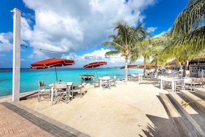 A beachside restaurant with outdoor seating, palm trees, and a view of the ocean. - Villa Coral Breeze - Paradise at Coral Estate (St. Marie)