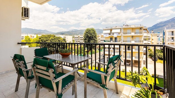 A balcony with a table and chairs, a potted plant, and a view of a residential area with buildings and mountains in the background. - Socrates Suites Open City Views in Kalamata (Kalamata)