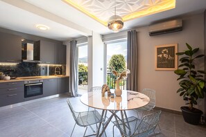 A modern kitchen with a built-in oven, a dining area with a round table and metal chairs, and a large window offering a view of greenery and a mountain. - Socrates Suites Open City Views in Kalamata (Kalamata)