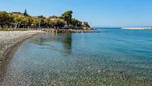 A pebble beach with clear water, a rocky shoreline, and buildings with red roofs in the background. - Socrates Suites Open City Views in Kalamata (Kalamata)