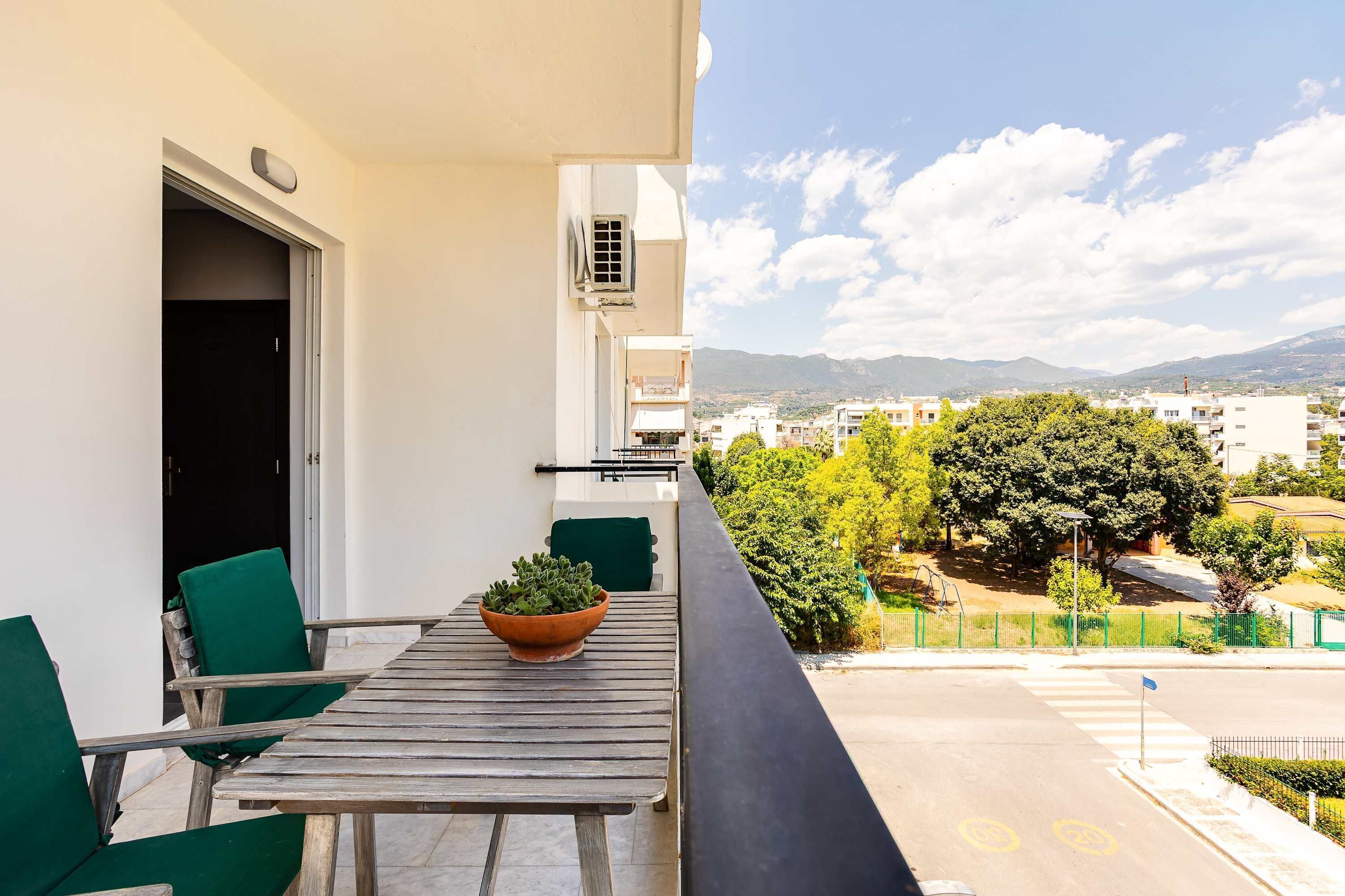 A balcony with a table and chairs, a potted plant, and a view of the city and mountains.