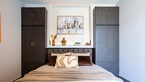 A bedroom with a bed, dark wooden cabinets, a cityscape painting, and a tufted headboard. - Socrates Suites Open City Views in Kalamata (Kalamata)