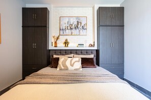 A bedroom with a bed, dark wooden cabinets, a cityscape painting, and a tufted headboard. - Socrates Suites Open City Views in Kalamata (Kalamata)