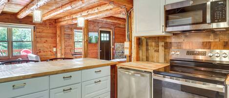 A kitchen with wooden beams, white cabinetry, a stainless steel microwave, and a built-in oven.