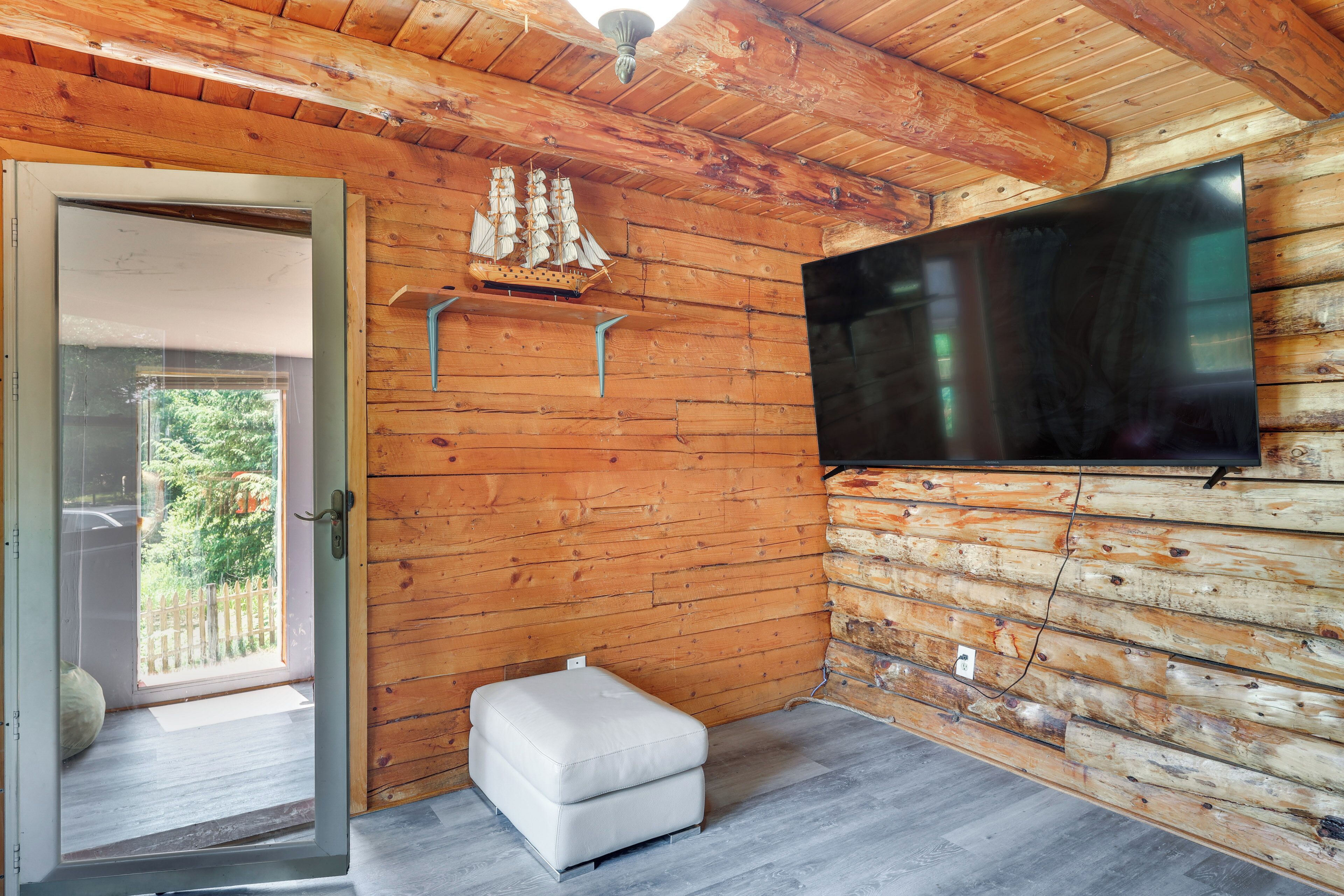 A wooden cabin interior with a television mounted on the wall, a small ottoman, and a model ship.
