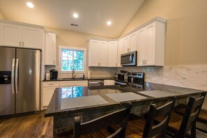 A modern kitchen with white cabinets, stainless steel appliances, and a large island with bar stools. - Modern Upper Retreat II 2 Suites Free Tix (Hendersonville)