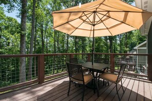 A wooden deck with a table and chairs, a large umbrella, and a view of a forested area. - Modern Upper Retreat II 2 Suites Free Tix (Hendersonville)