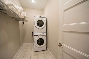 A laundry room with two stacked washing machines, a metal drying rack with clothes, and a white door. - Druid Hills Retreat II Sleeps 8 Free Tix (Hendersonville)