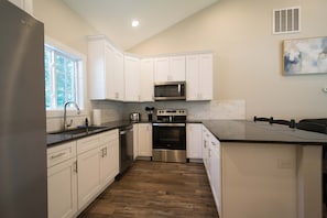 A kitchen with white cabinets, stainless steel appliances, a large island, and a window. - Druid Hills Retreat II Sleeps 8 Free Tix (Hendersonville)