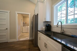 A kitchen with white cabinets, a stainless steel refrigerator, a sink with a modern faucet, and a window with a view of trees. - Druid Hills Retreat II Sleeps 8 Free Tix (Hendersonville)