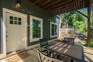 A covered patio with a table and chairs, a welcome mat, and a stone wall in the background. - Druid Hills Retreat II Sleeps 8 Free Tix (Hendersonville)