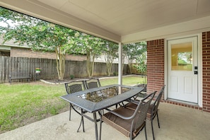 Un patio couvert avec une table et des chaises en métal, un mur en briques et une clôture en bois en arrière-plan.