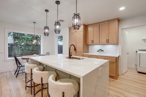 A modern kitchen with a large island, bar stools, pendant lighting, and wooden cabinets. - Near Splashtown & The Woodlands! Poolside Retreat (Tomball)