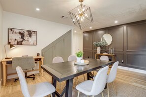 A modern dining area with a dark wooden table, grey upholstered chairs, a geometric pendant light, and a minimalist decor. - Near Splashtown & The Woodlands! Poolside Retreat (Tomball)