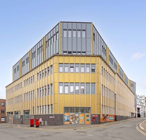 A corner building with a yellow facade, multiple windows, and a brick base. - Student Only The Paper Works (Sheffield)
