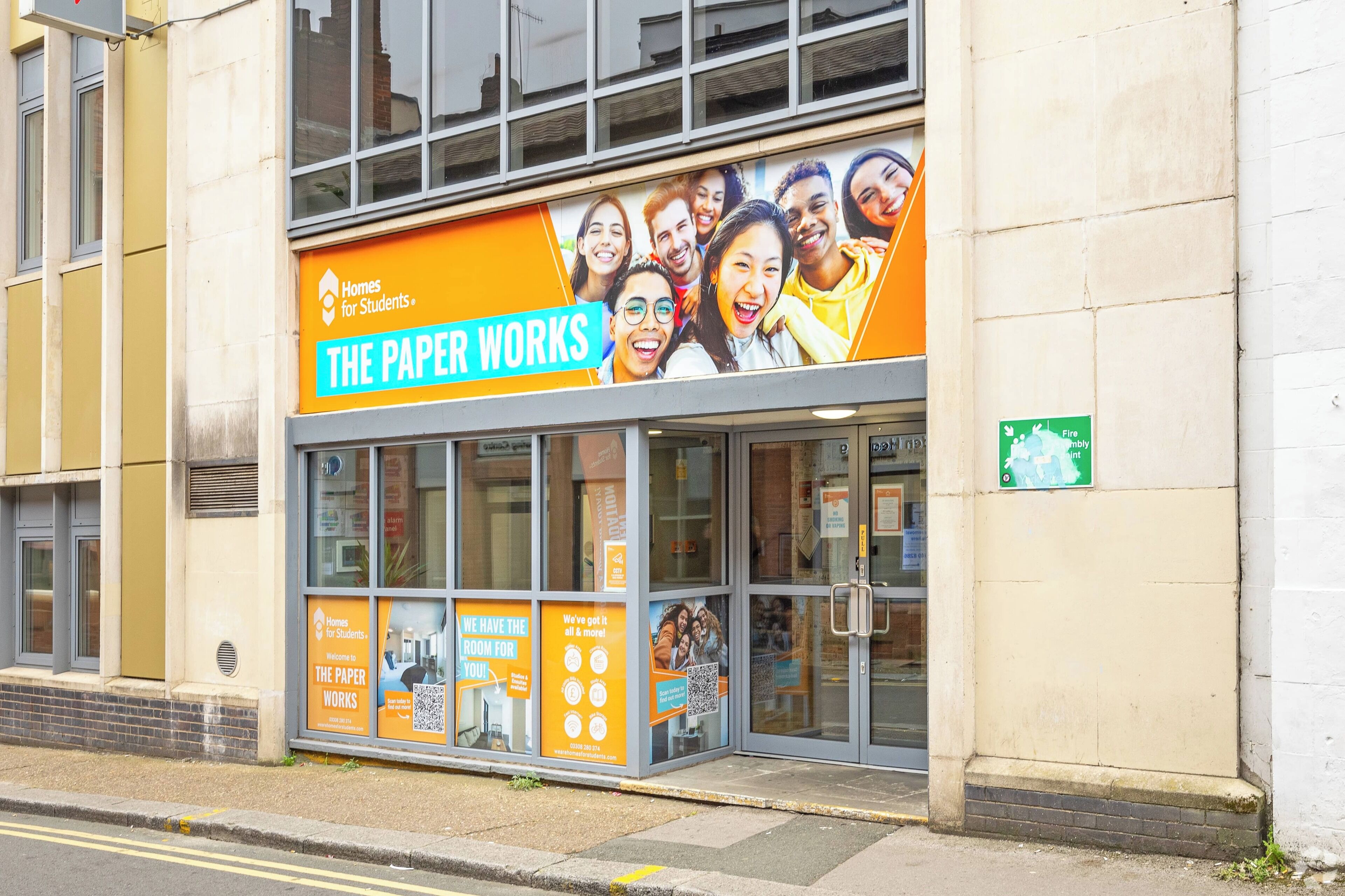 A building with a large sign advertising 'The Paper Works' and a fire assembly point sign.