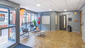 Ein modernes Interieur mit einem Fischgrätparkett, einer Sitzecke mit Tisch und Stühlen, einer Topfpflanze und einer Tür mit einem Brandmelder.