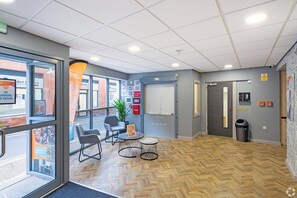 Ein modernes Interieur mit einem Fischgrätparkett, einer Sitzecke mit Tisch und Stühlen, einer Topfpflanze und einer Tür mit einem Brandmelder.