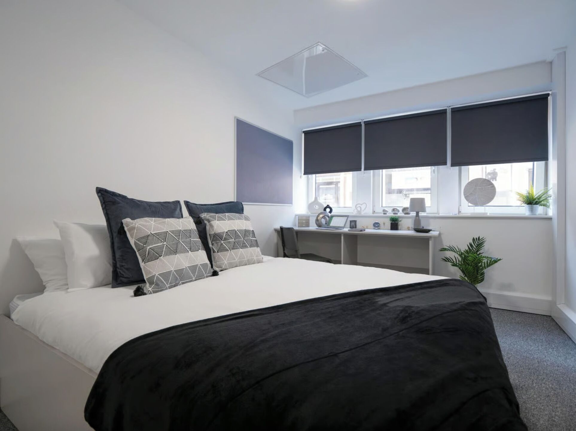 A modern bedroom with a bed, bedside tables, a desk, and a window with blinds.