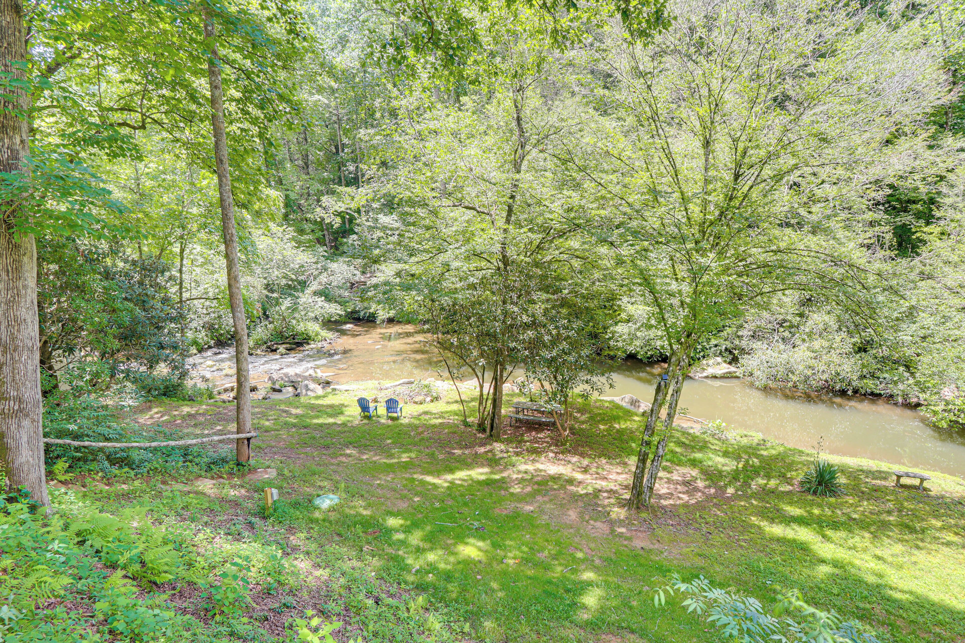 A natural setting with a river, trees, and outdoor seating.