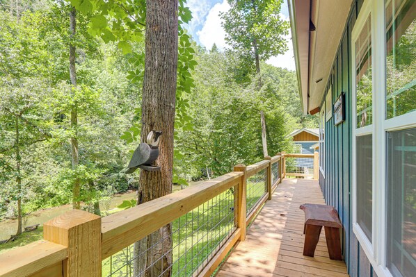 A wooden deck with a metal railing, overlooking a forested area with a bird feeder on a tree.