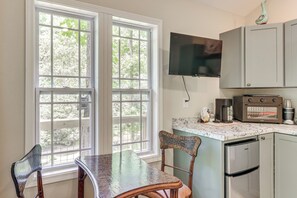 A kitchen with a dining table, chairs, a television, and a coffee maker.