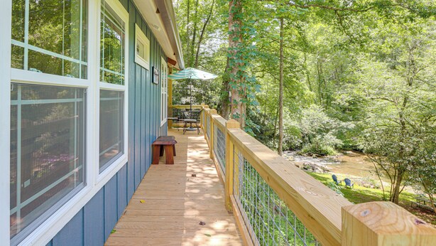 A wooden deck with a railing, overlooking a forested area with a table and chairs. - On-site Trout Stream & Fire Pit! Murphy Tiny Home (Murphy)
