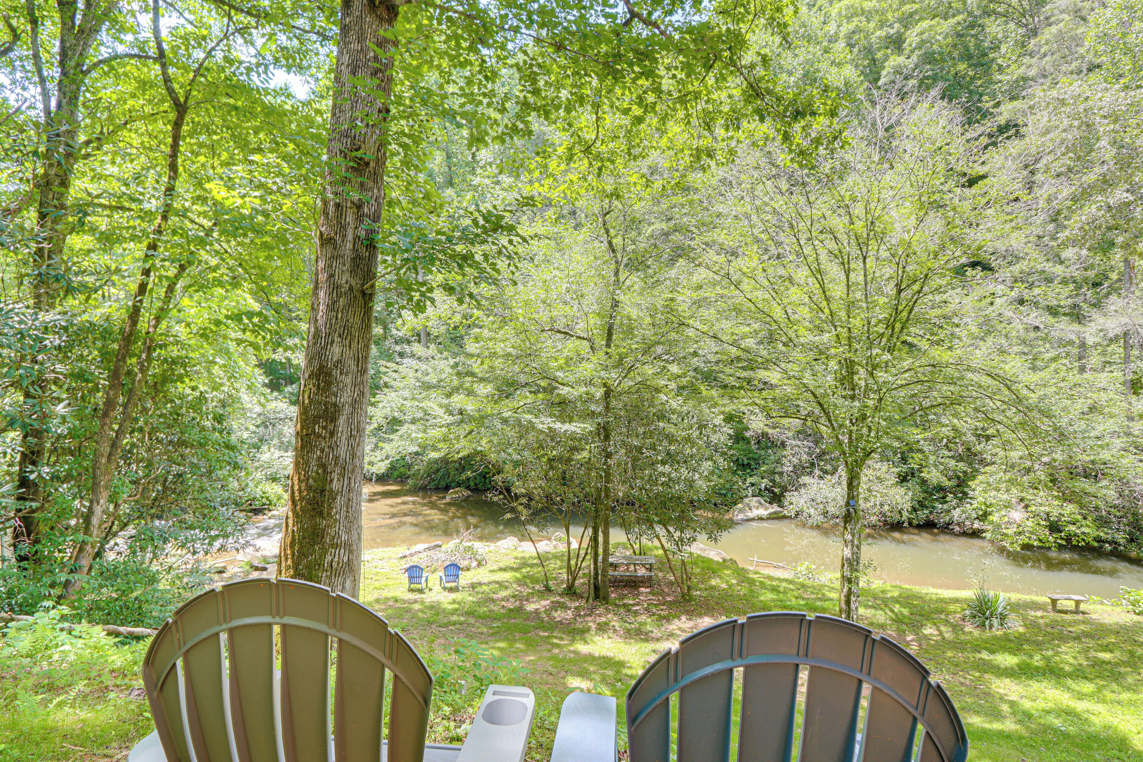 A view of a forested area with a river, two chairs, and a picnic table.
