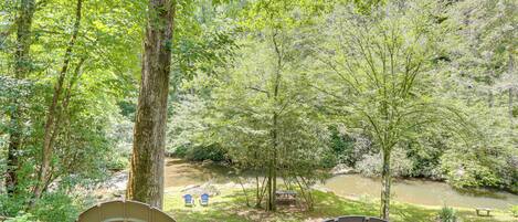 A view of a forested area with a river, two chairs, and a picnic table.