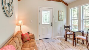 A living room with a wooden ceiling, a white door, a sofa, a table, and chairs. - On-site Trout Stream & Fire Pit! Murphy Tiny Home (Murphy)