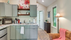 A kitchen with a central island, a dining area with a sofa, and a view of a garden through a window. - On-site Trout Stream & Fire Pit! Murphy Tiny Home (Murphy)