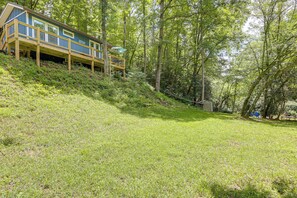 A house with a wooden deck and a covered area, surrounded by a grassy slope and trees. - On-site Trout Stream & Fire Pit! Murphy Tiny Home (Murphy)