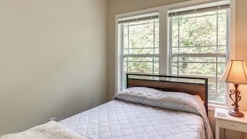Ein Schlafzimmer mit einem Bett, einem Nachttisch mit Lampe und einem Fenster mit Blick auf Bäume.