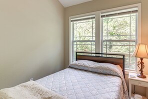 A bedroom with a bed, a bedside table with a lamp, and a window with a view of trees. - On-site Trout Stream & Fire Pit! Murphy Tiny Home (Murphy)