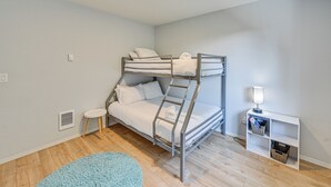 A bunk bed room with a small table, a lamp, and a shelf with baskets.