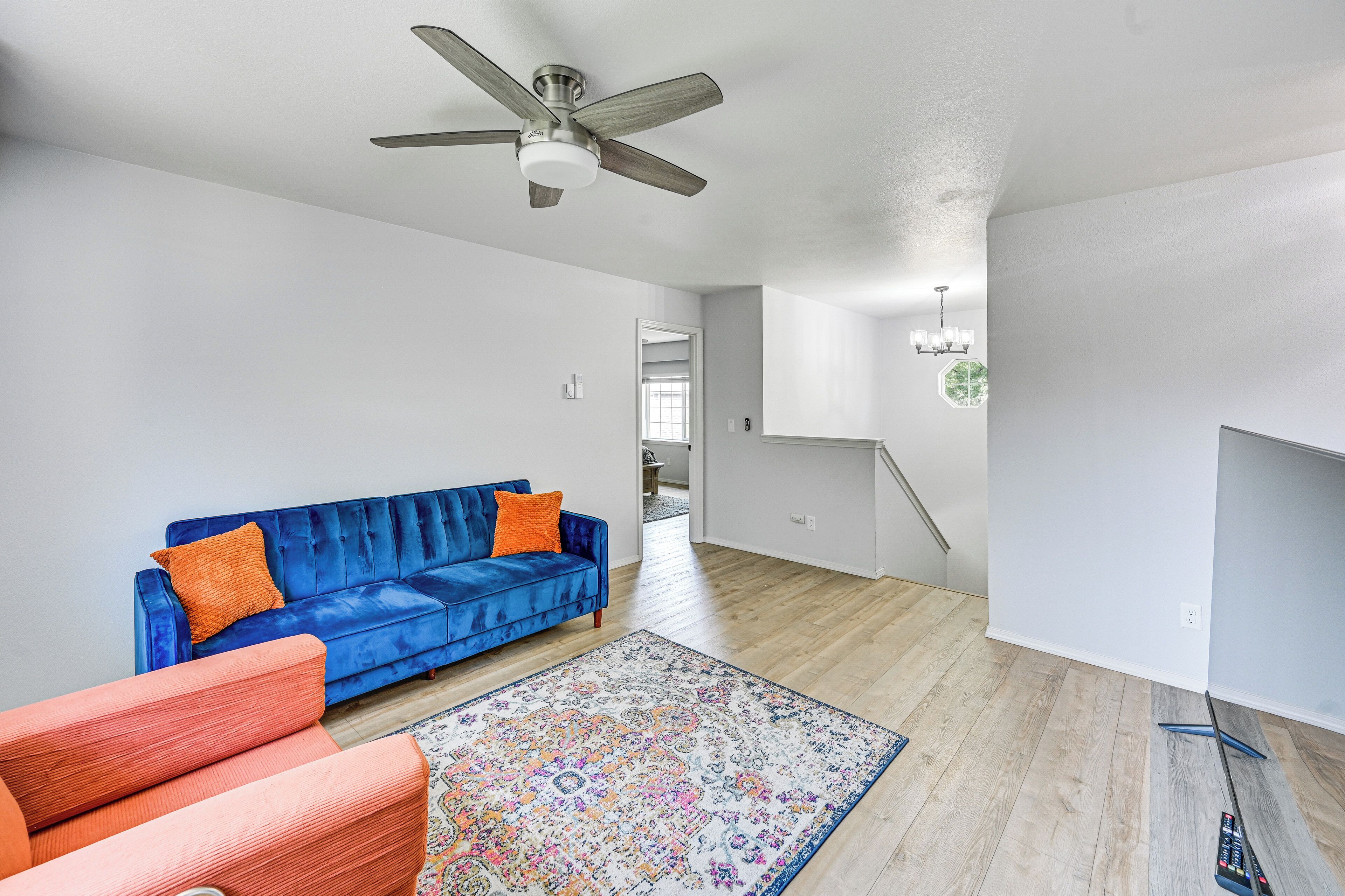 Un salon moderne avec un canapé bleu, un tapis à motifs et un ventilateur de plafond.