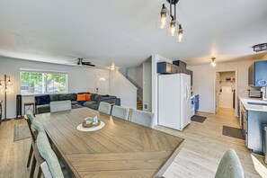 A modern kitchen with a central island, a dining area with a wooden table, and a living room with a sofa and a ceiling fan.