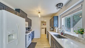 Une cuisine moderne avec des appareils électroménagers blancs, des meubles de rangement sombres et une grande fenêtre.