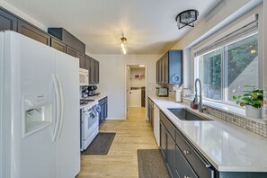 Cozinha moderna com eletrodomésticos brancos, armários escuros e uma janela grande.