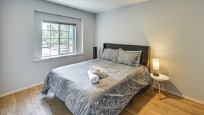 Une chambre à coucher avec un lit, une table de chevet avec une lampe, une fenêtre et une vue sur l’extérieur.