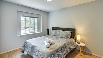 A bedroom with a bed, a bedside table with a lamp, a window, and a view of the outside.