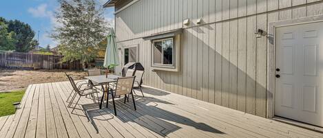 A wooden deck with a table and chairs, a white door, and a window.