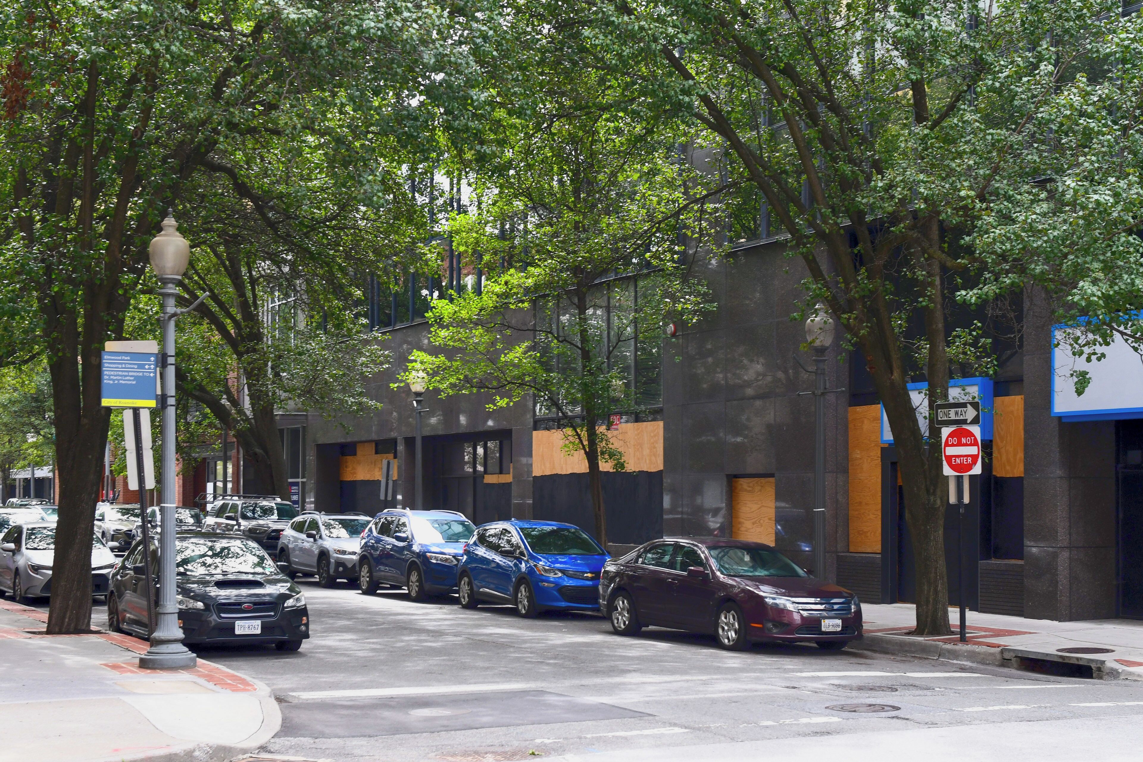 A street lined with parked cars and trees, a pedestrian bridge, and a building with a 'DO NOT ENTER' sign.