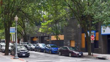 A street lined with parked cars and trees, a pedestrian bridge, and a building with a 'DO NOT ENTER' sign.